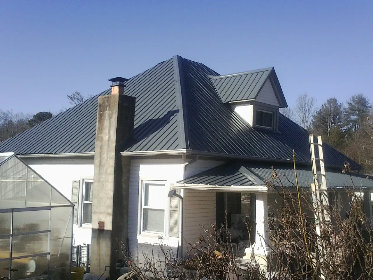 Dark blue standing seam metal roof on a white farmhouse with dormer — Slate & Tile Roof Repair by Roofing Brothers in Maryknoll