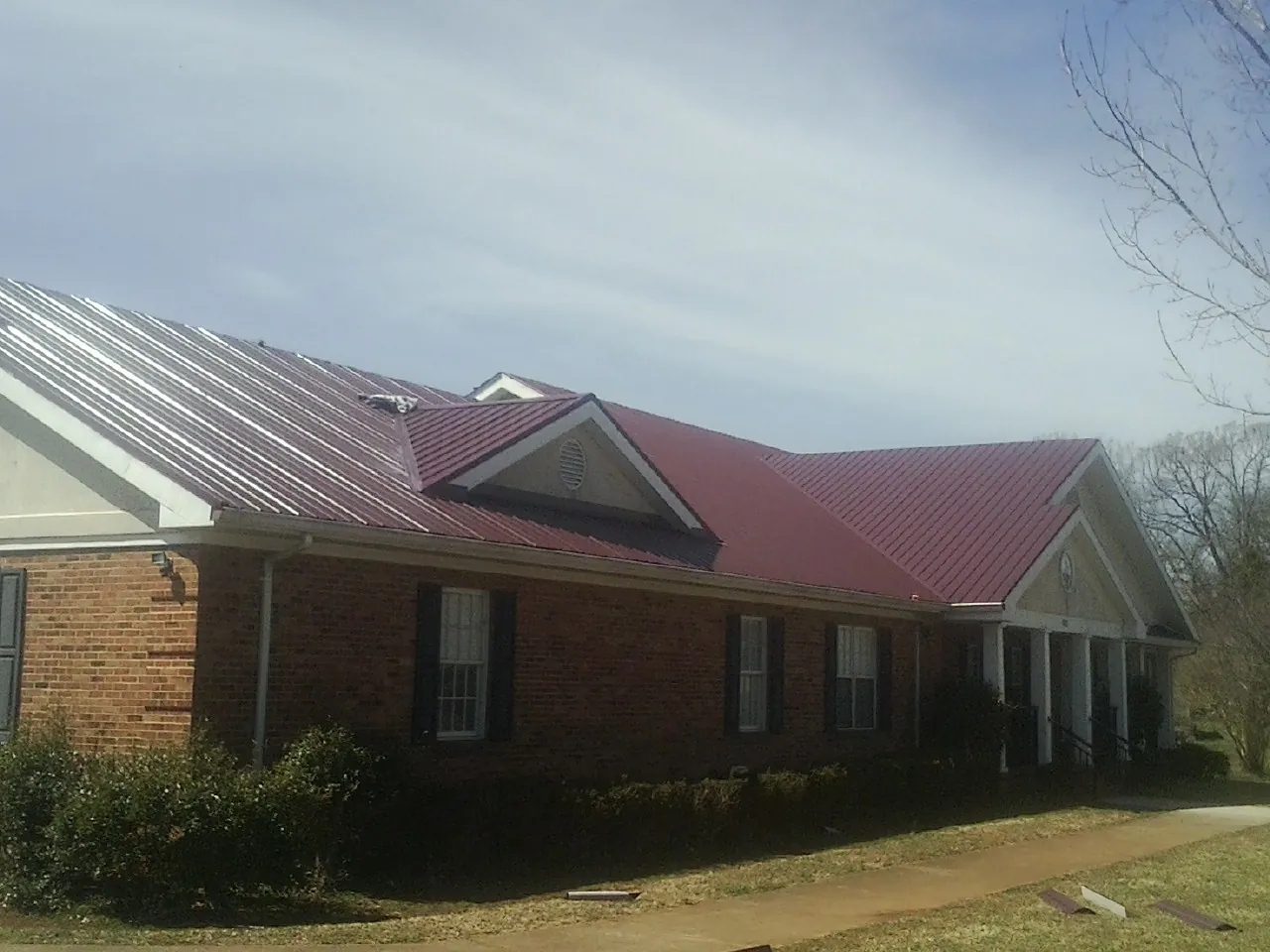 Red metal roof with gabled entries on a long brick building, from a Hail Damage Roof Repair job in Maryknoll
