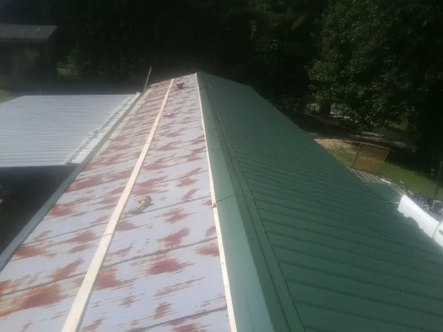 Old rusted panels beside newly installed green metal roofing — Wind Damage Roof Repair by Roofing Brothers in Maryknoll
