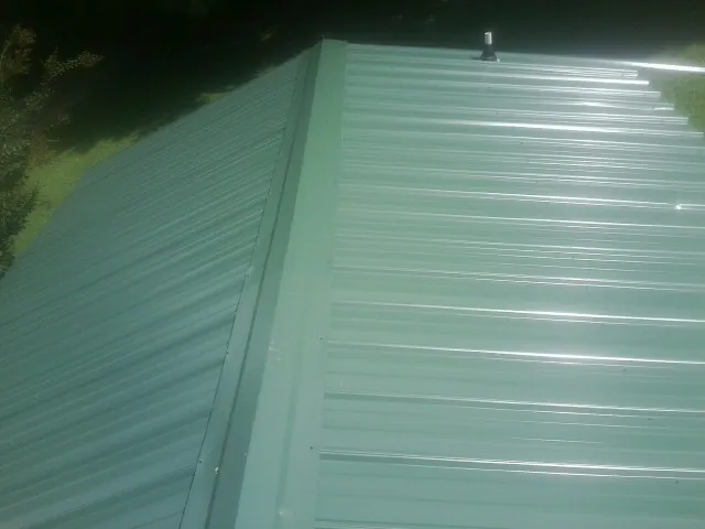 New green metal panels meeting at the ridge of a roof — Flat Roof Repair work by our crew in Maryknoll