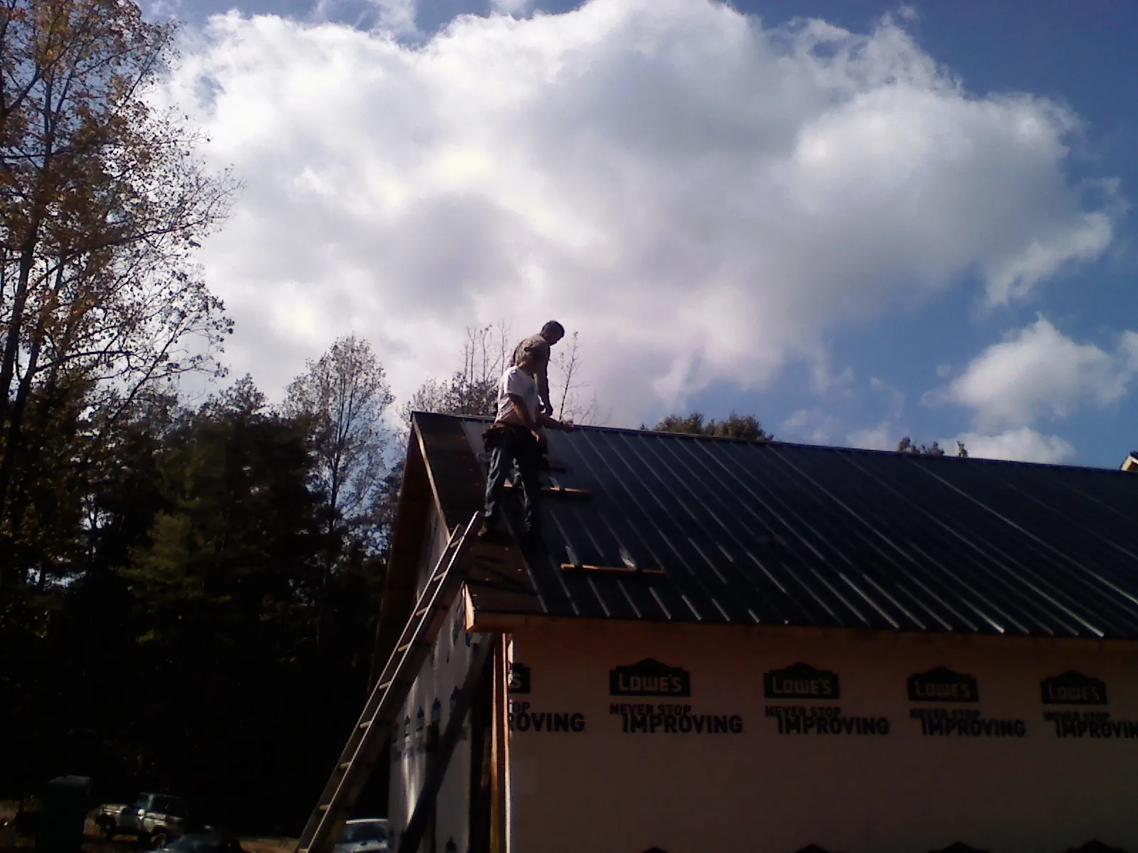 Roofer fastening dark metal panels high against a cloudy sky, from a Roof Inspection job in Maryknoll