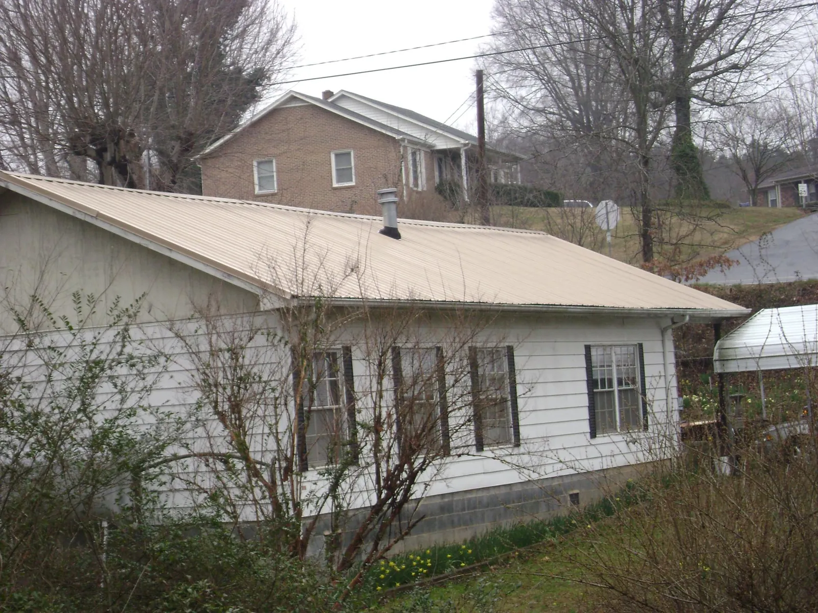 Tan metal roof on a white sided house set into a hillside — Commercial Roofing by Roofing Brothers in Maryknoll