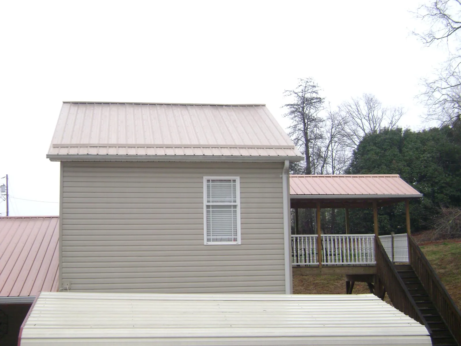 Tan metal roofs on a two story addition and attached porch, from a Roof Replacement job in Maryknoll